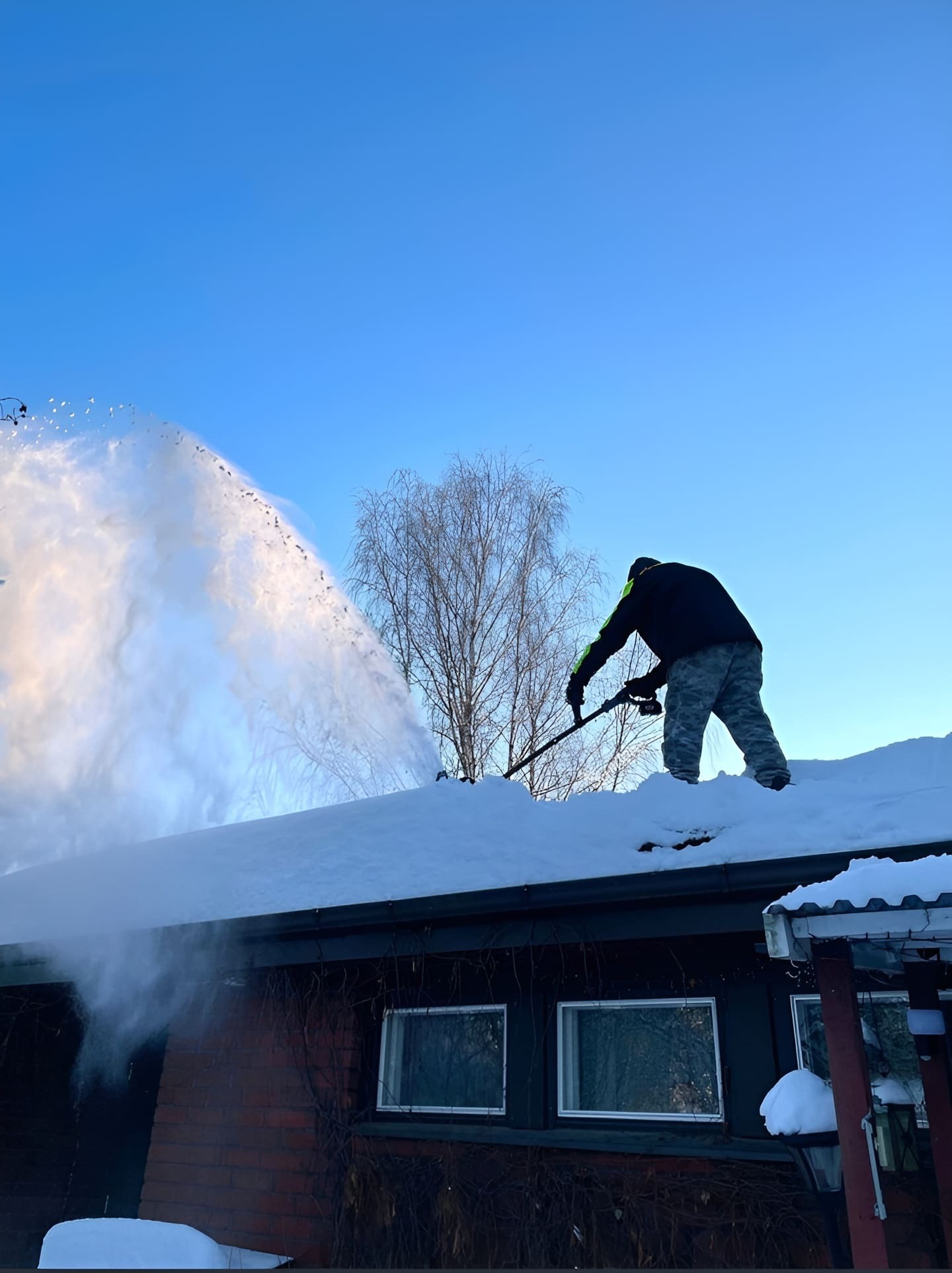 Déneigement manuel d'un toit résidentiel.
